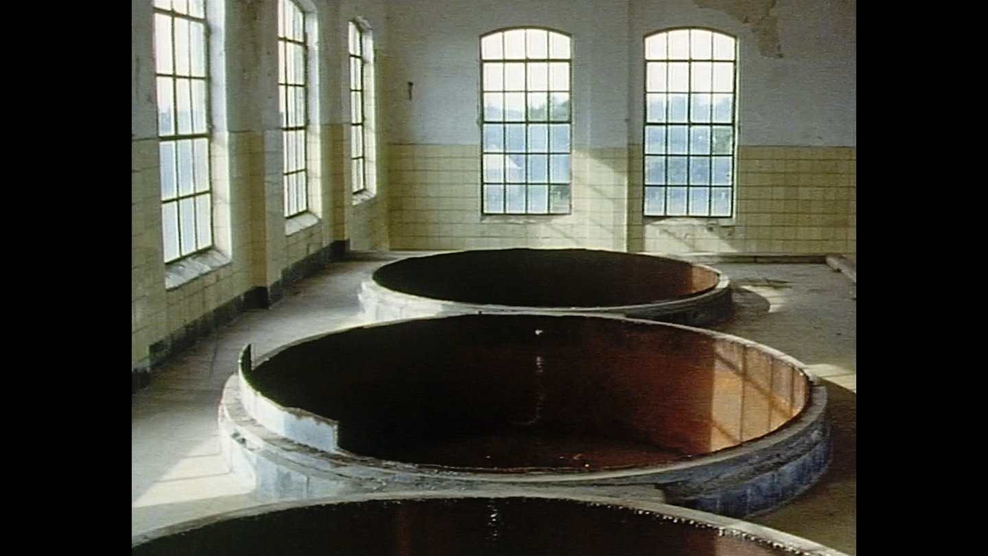 Filmstill von "Afscheid", Drei große runde Becken, fast gänzlich im Boden eingelassen, in einem hellen Raum mit hohen Fenstern und weißen Kacheln an den Wänden
