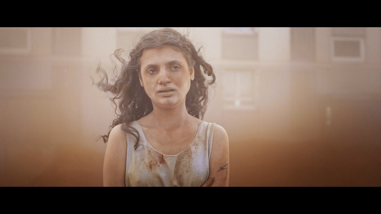 Filmstill aus ALPHA: Eine mit staub überdeckte Frau blickt zur Kamera.