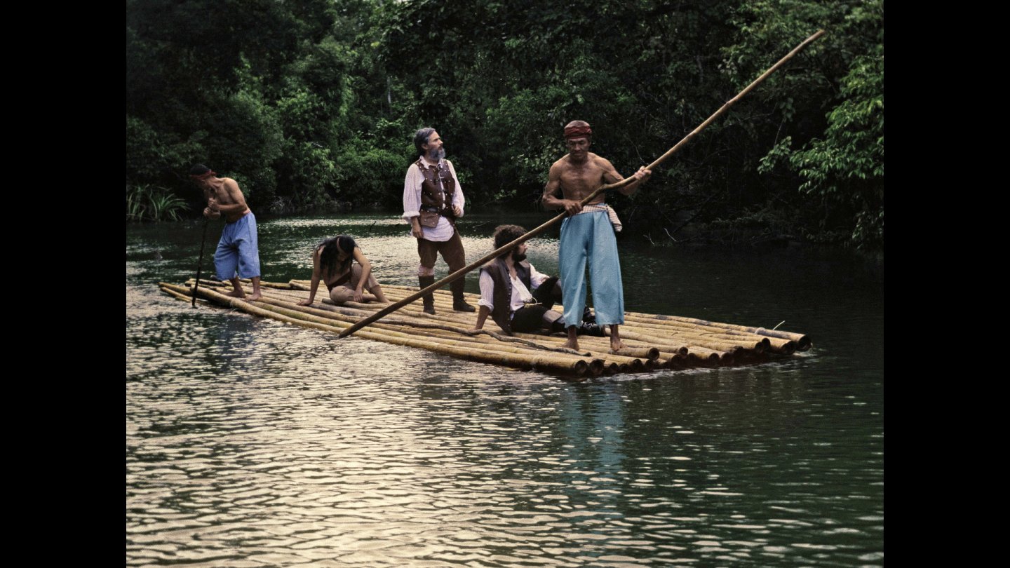 4 Männer fahren mit einem selbstgebauten Boot aus Holzstämmen über das Wasser.