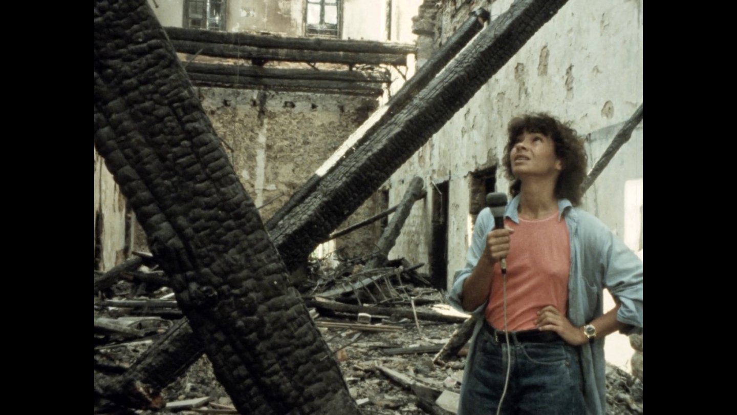 FIlmstill Jocelyne Saab: Frau mit Mikrofon steht in einem ausgebrannten, zerstörten Gebäude und blickt nach oben