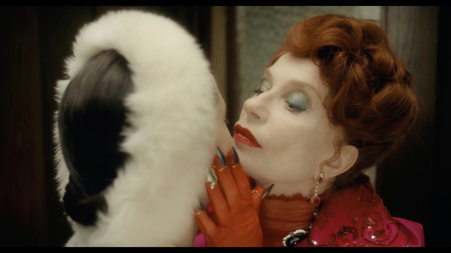 Filmstill Die Blutgräfin, The Blood Countess von Ulrike Ottinger, Isabell Huppert als Blutgräfin mit rotem, lockigem Haar und rotem Lippenstift trägt rote Handschuhe und hält das Gesicht einer anderen Frau, die ein weißes Fell Stirnband trägt, ganz nah vor ihr Gesicht