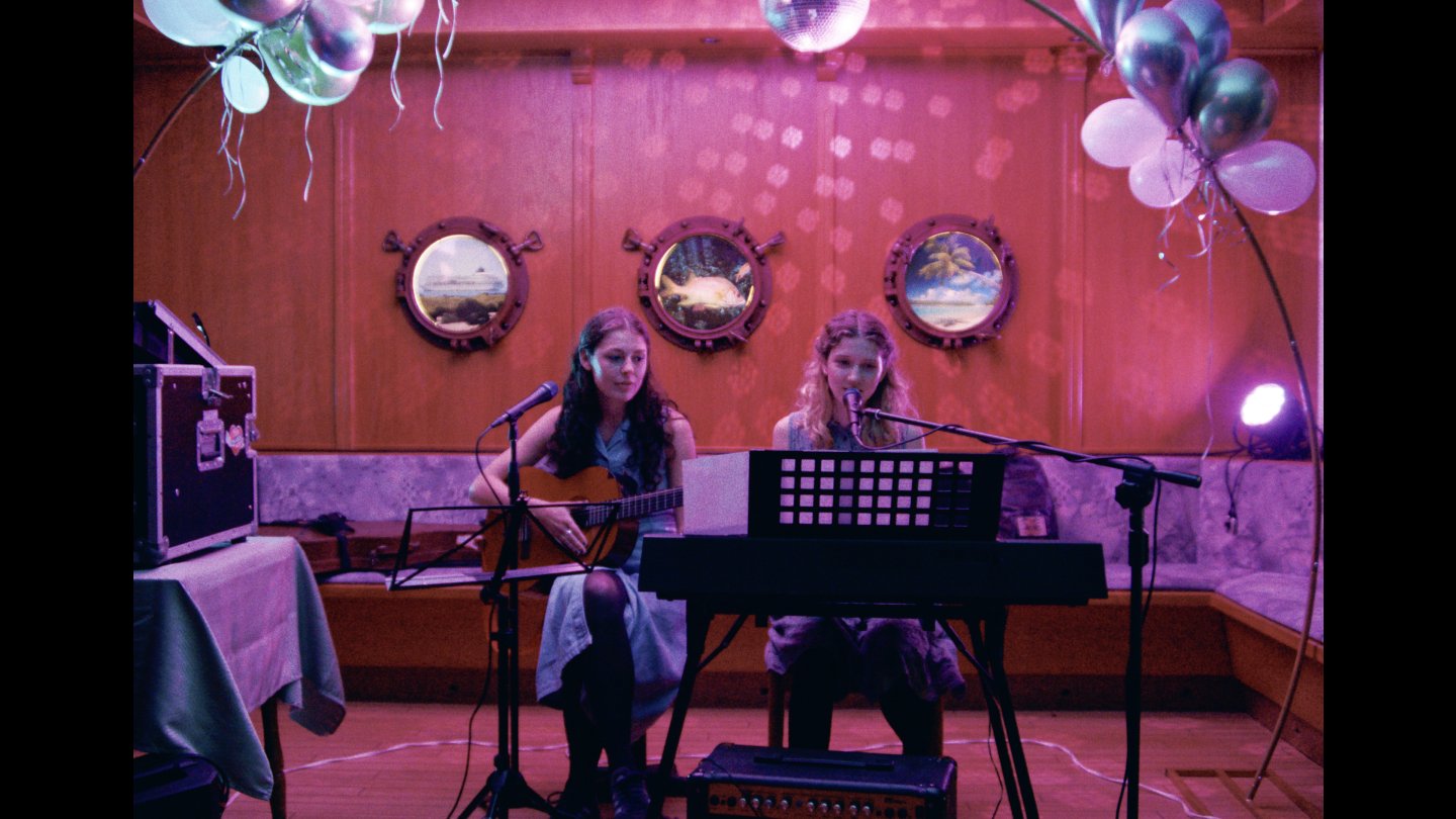 2 junge Frauen sitzen auf einer Bühne, sie sind dabei ein Musikstück zu performen.