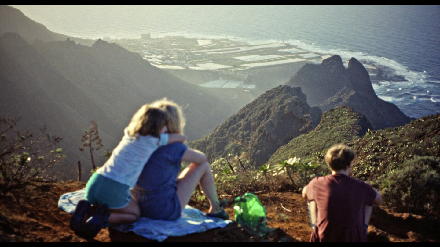 3 Menschen sitzen mit dem Rücken zur Kamera und blicken auf eine Landschaft.