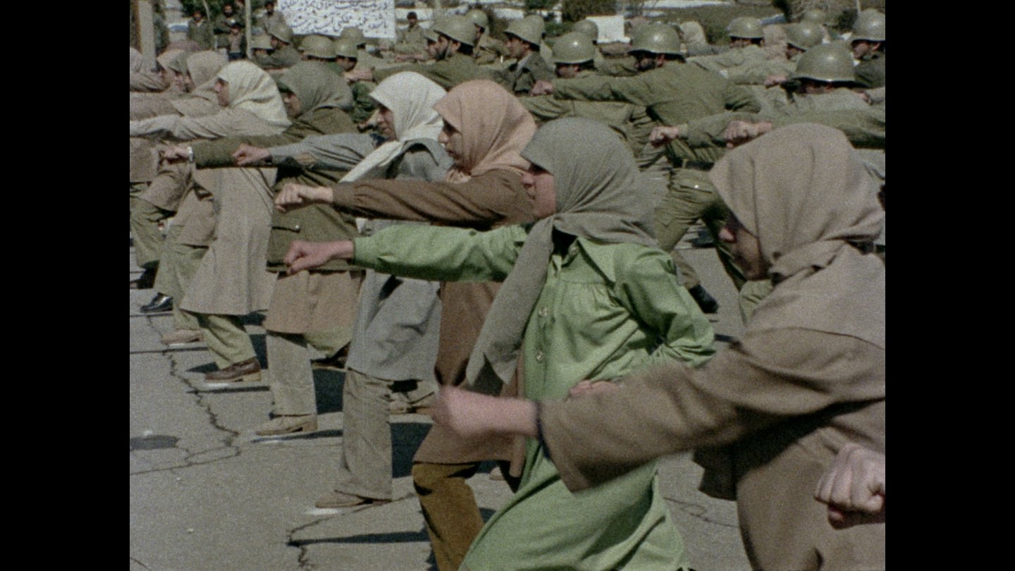 Filmstill Jocelyne Saab: Gruppe von Frauen mit Kopftüchern und Mänteln steht in einer Reihe und streckt die Arme nach vorne aus