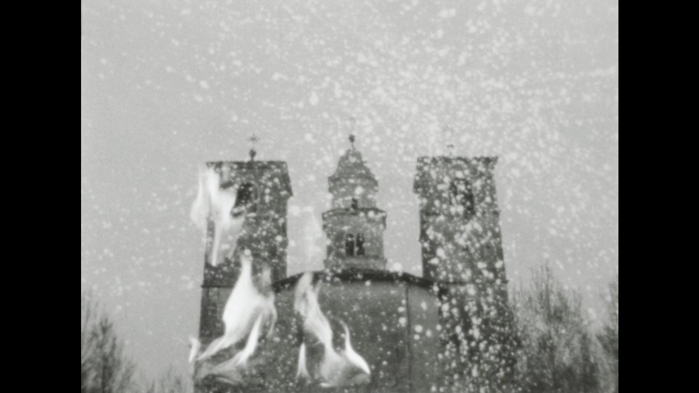 Kirchengebäude mit zwei Türmen im Hintergrund und Flammen im Vordergrund bei Schneefall