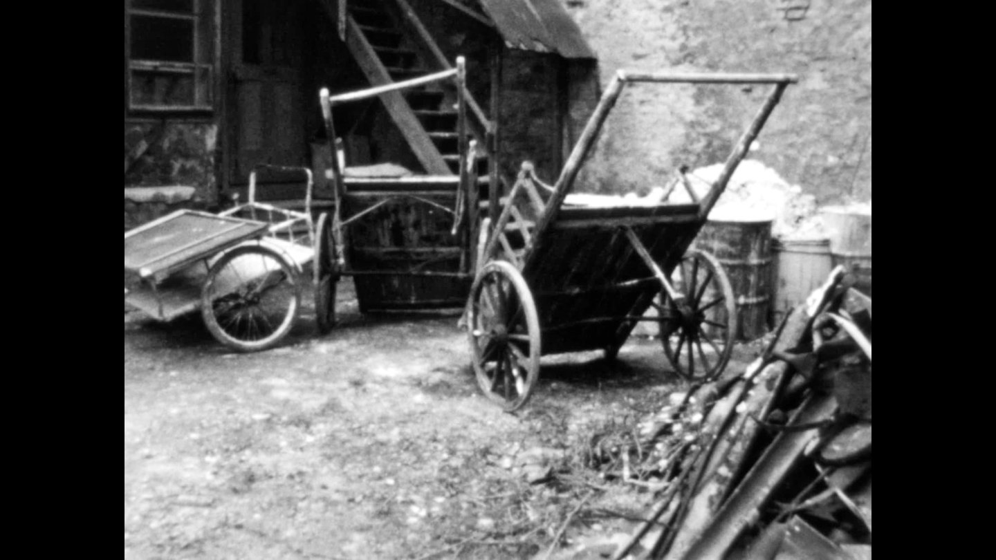 Zwei alte Holzwagen mit großen Speichenrädern stehen in einem Hof vor einer Mauer