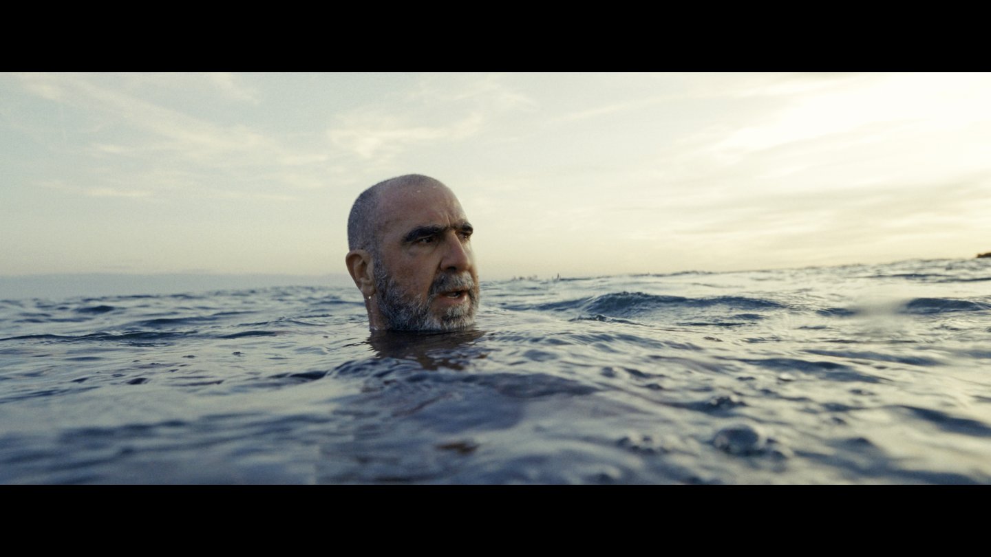 Ein Mann befindet sich in einem Gewässer, wahrscheinlich ein Meer, zu sehen ist nur sein Kopf. Er wirkt verwirrt, das Wasser unruhig.