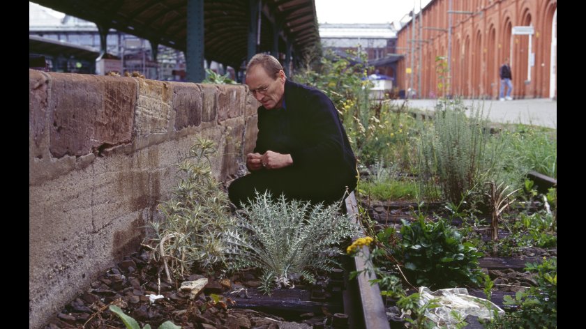 Filmstill aus LOIS WEINBERGER - RUDERAL SOCIETY: Ein Mann hockt in einem Garten.