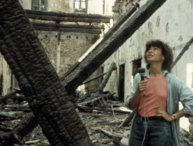 FIlmstill Jocelyne Saab: Frau mit Mikrofon steht in einem ausgebrannten, zerstörten Gebäude und blickt nach oben
