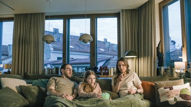 Eine dreiköpfige Familie in einer Wohnung, sie sitzen auf einem Sofa. 