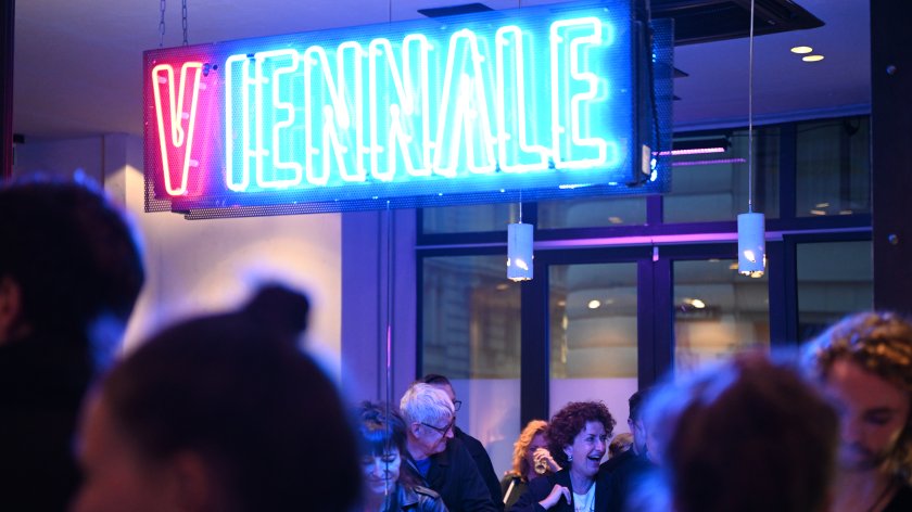 Ein leuchtender VIENNALE Schriftzug über einer Bar.