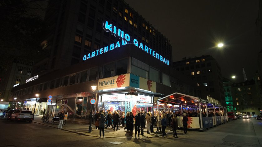Nächtliche Straßenszene mit beleuchtetem Kino-Gebäude "Kino Gartenbau" und Menschen vor dem Eingang