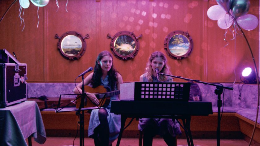 2 junge Frauen sitzen auf einer Bühne, sie sind dabei ein Musikstück zu performen.