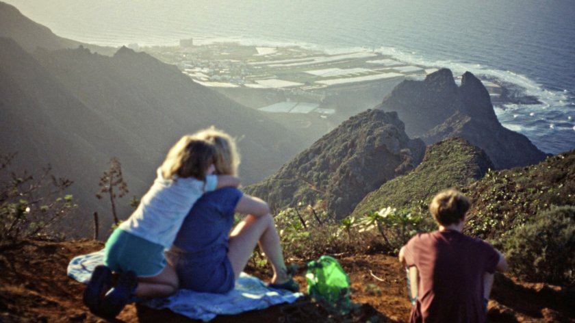 3 Menschen sitzen mit dem Rücken zur Kamera und blicken auf eine Landschaft.