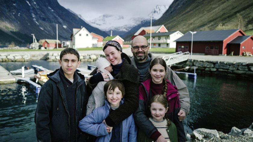 Ein Familienporträt, abgebildet sind fünf Kinder und 2 Erwachsene. Sie stehen vor einem Gewässer und lächeln in die Kamera.