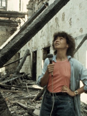FIlmstill Jocelyne Saab: Frau mit Mikrofon steht in einem ausgebrannten, zerstörten Gebäude und blickt nach oben