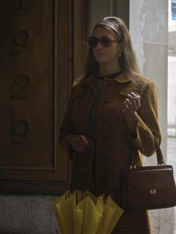 Eine Frau steht in einem Eingangstor, es regnet hinter ihr, sie trägt Sonnenbrille und hat eine Zigarette in der Hand.